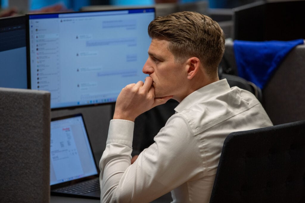 Op de afbeeding zie je een mannelijke collega. Hij is aan het werk achter zijn laptop en beeldschermen.