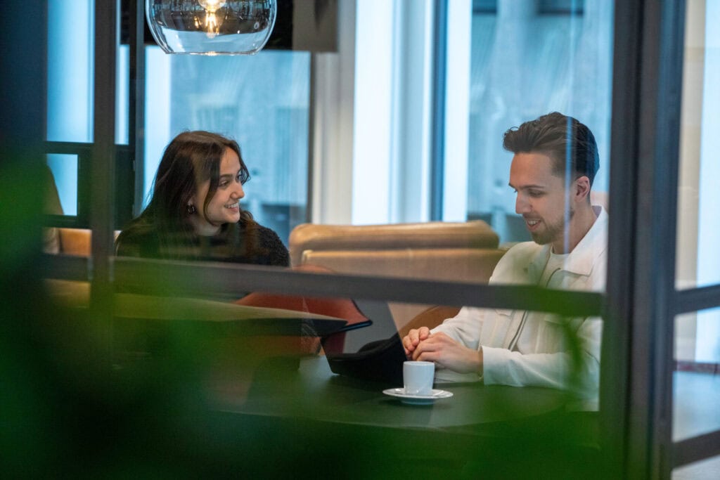 Collega's zitten in te vergaderen in het kantoor. De man zit achter zijn laptop en ze lachen allebij