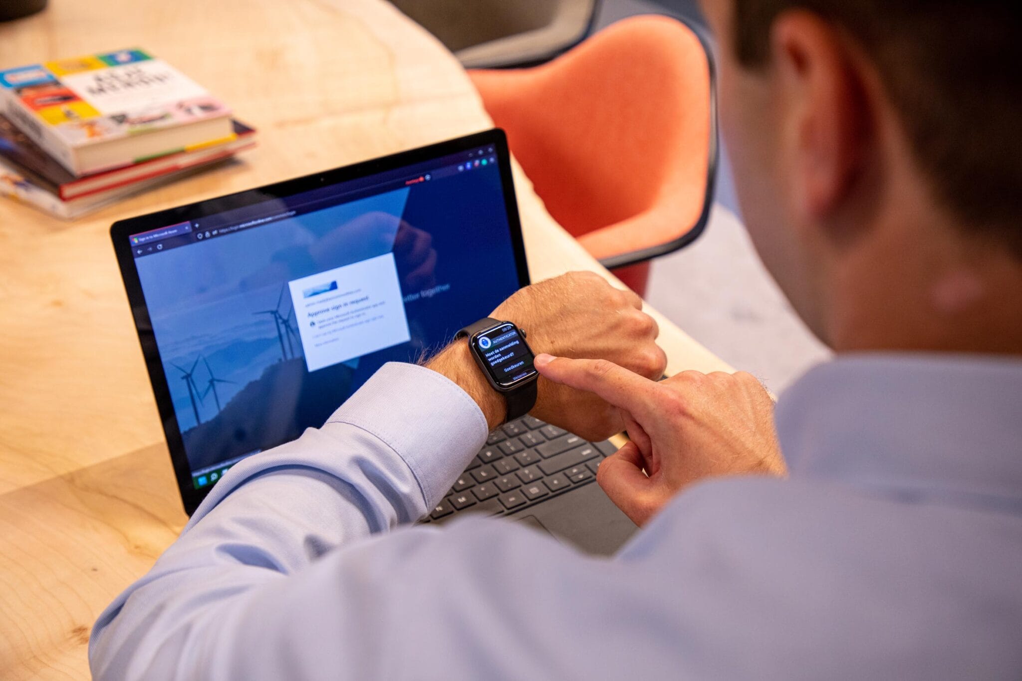 Iemand achter een laptop die een multifactor authenticatie op zijn horloge moet doen om in te loggen