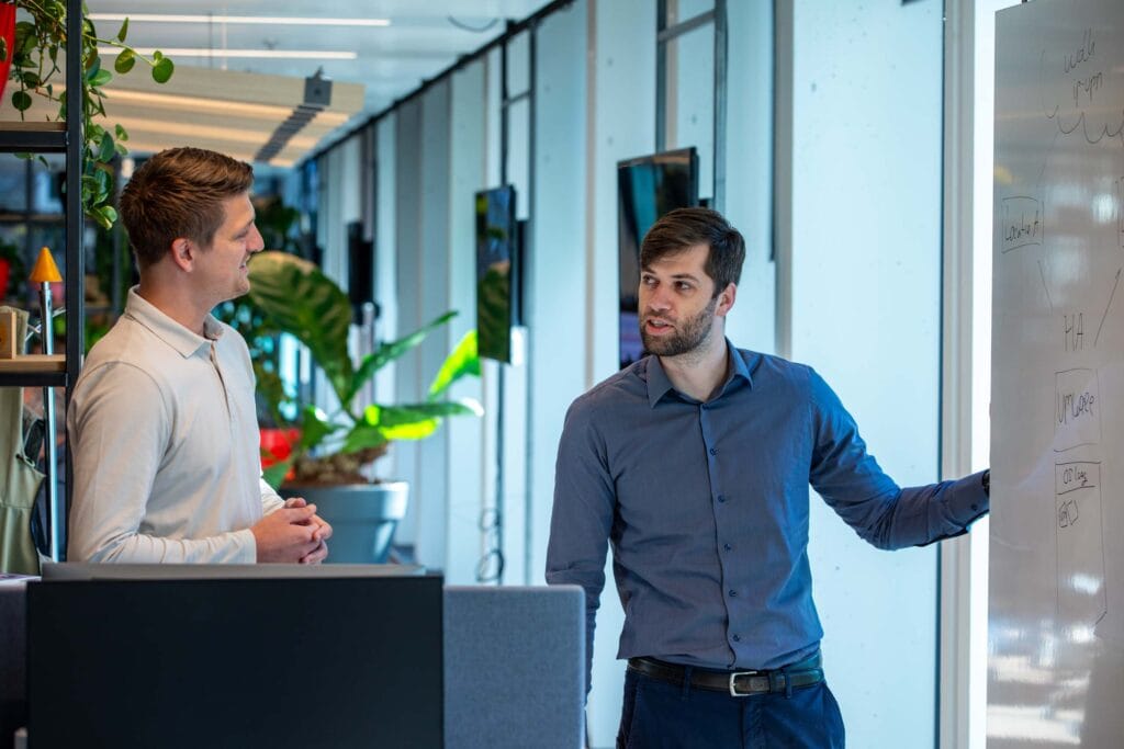 Twee mannen hebben op kantoor bij een whiteboard een overleg.