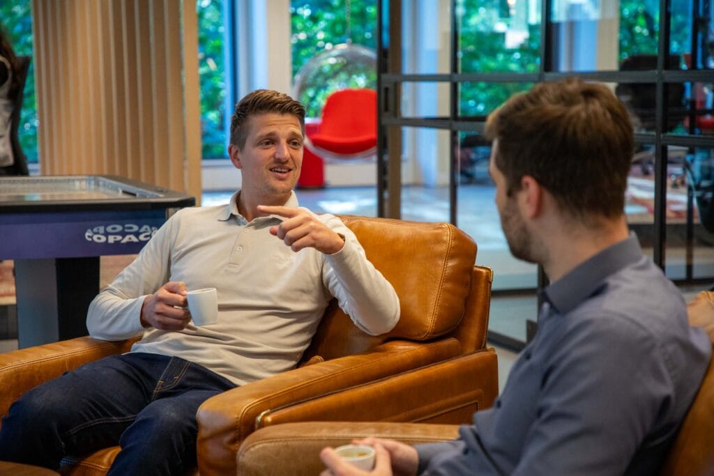 Twee mannen in het kantoor zijn met elkaar in gesprek. De ene man wijst met zijn vinger