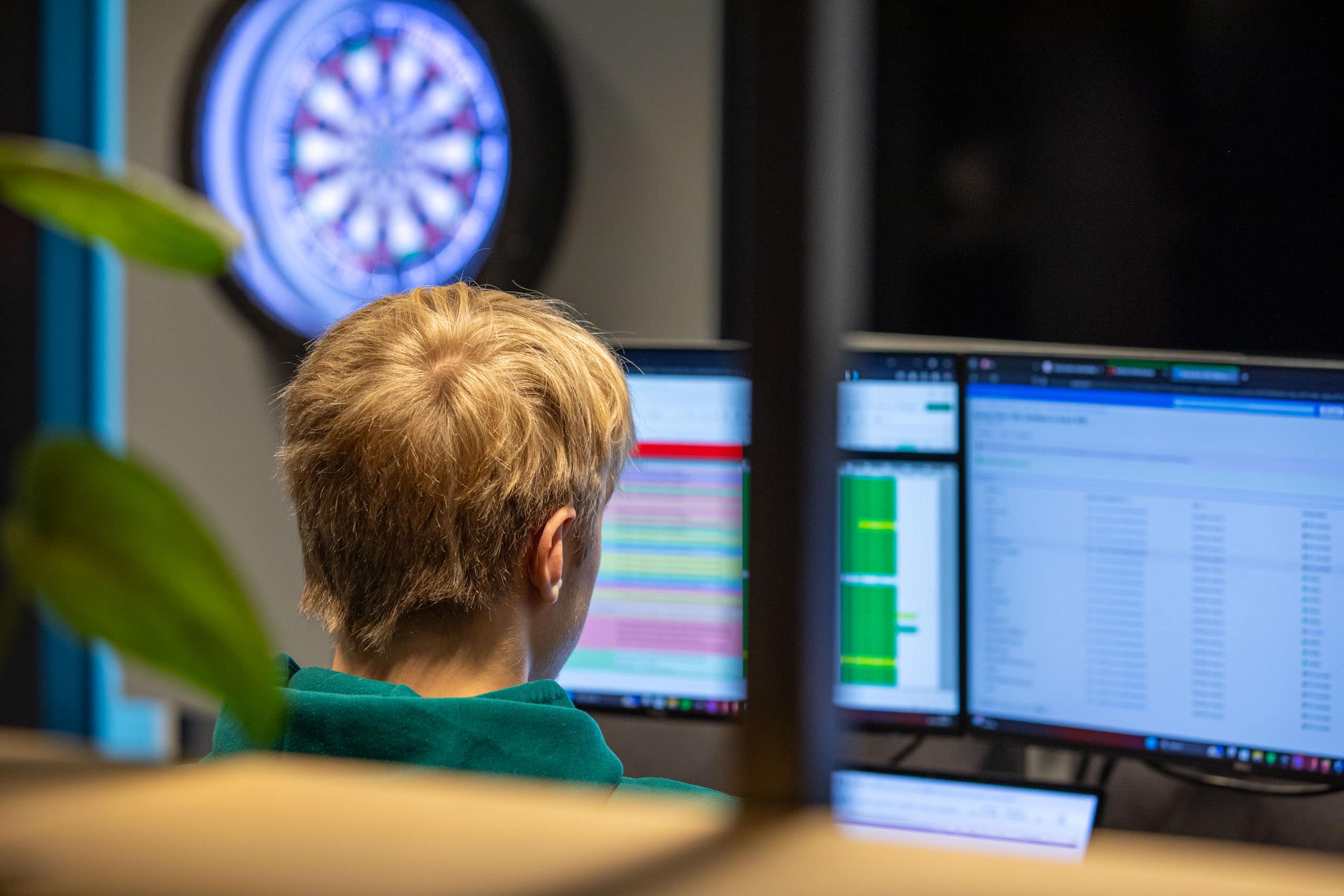 Man in op kantoor aan het scherm achter een scherm. In de achtergrond staat een dartboard.